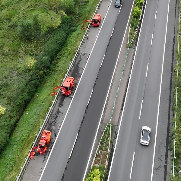航拍实拍高速公路绿化养护施工现场，多台津克 JK571 多功能修剪机械沿路侧开展绿篱边坡修剪作业，高速主线车辆正常通行，展示高速绿化作业单元化、多设备协同机械化养护实景。